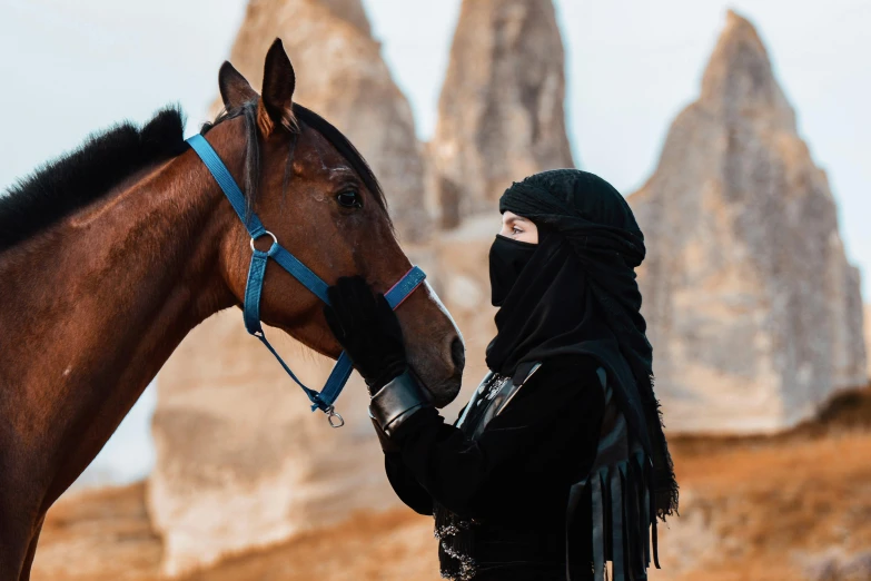 a woman in a black hijab is leading a brown horse