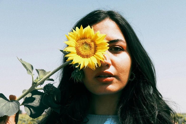 a woman holding up a sunflower to her eye