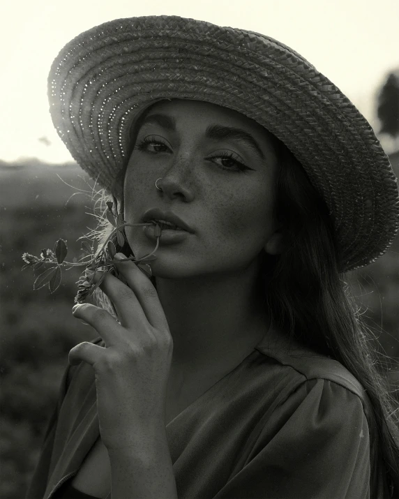 woman in a straw hat blows dandelion off of her nose