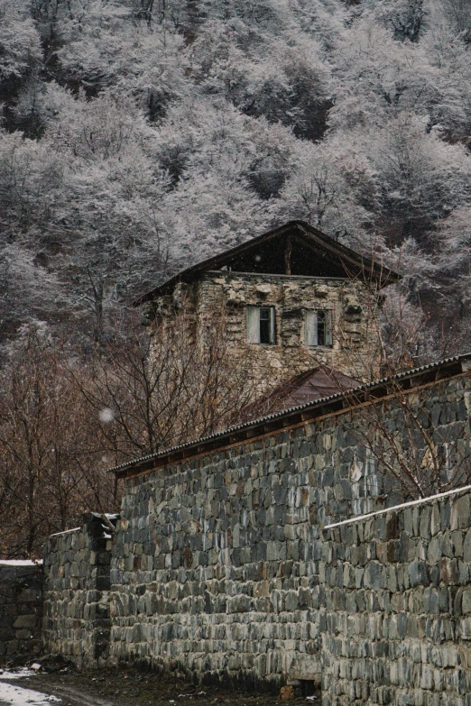 an old building near a stone wall in a snowy mountainside