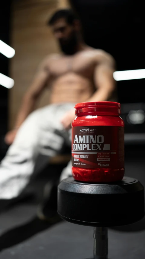 a man sitting down next to a red jar of protein