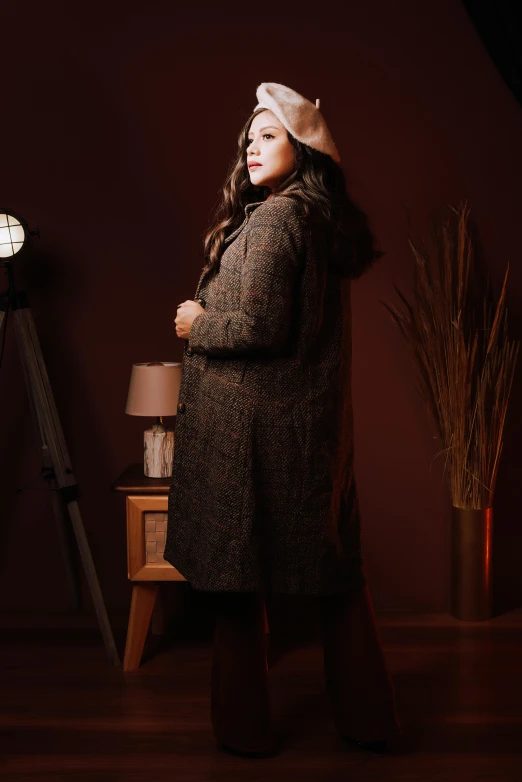 a woman wearing a coat standing on a wooden floor in front of a lamp