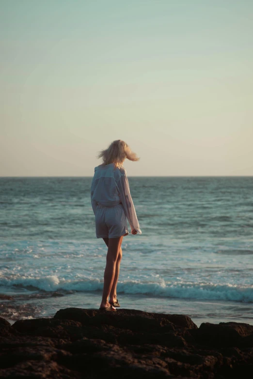 a woman standing on top of a rocky shore by the ocean