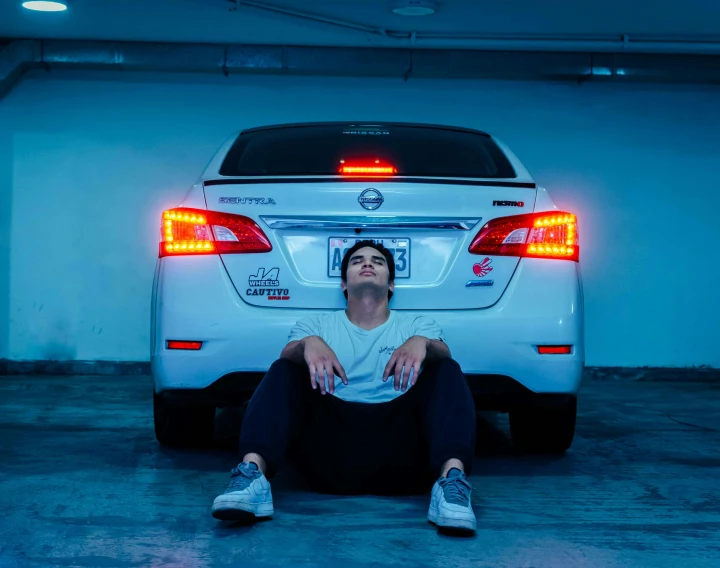 a man sitting on the ground under a car