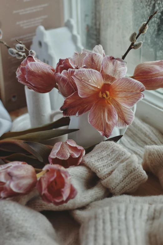 some pink flowers sitting in a white vase by a window