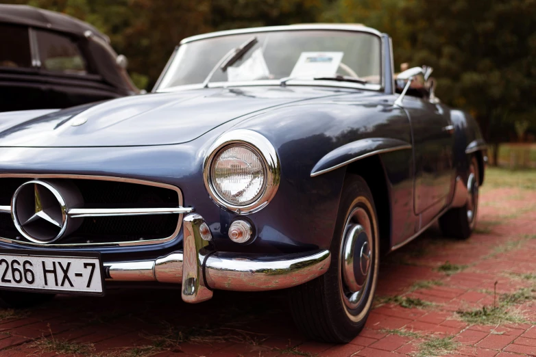 vintage convertible parked in the dirt with a classic car nearby