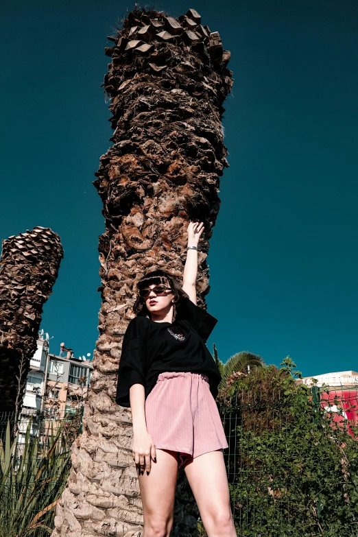 woman in pink shorts standing next to a large palm tree