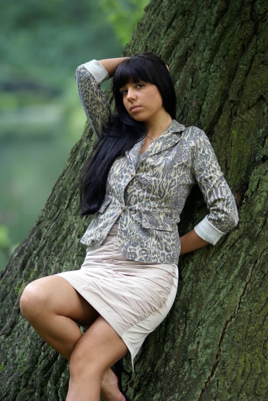 a girl sitting against a tree wearing a shirt and skirt