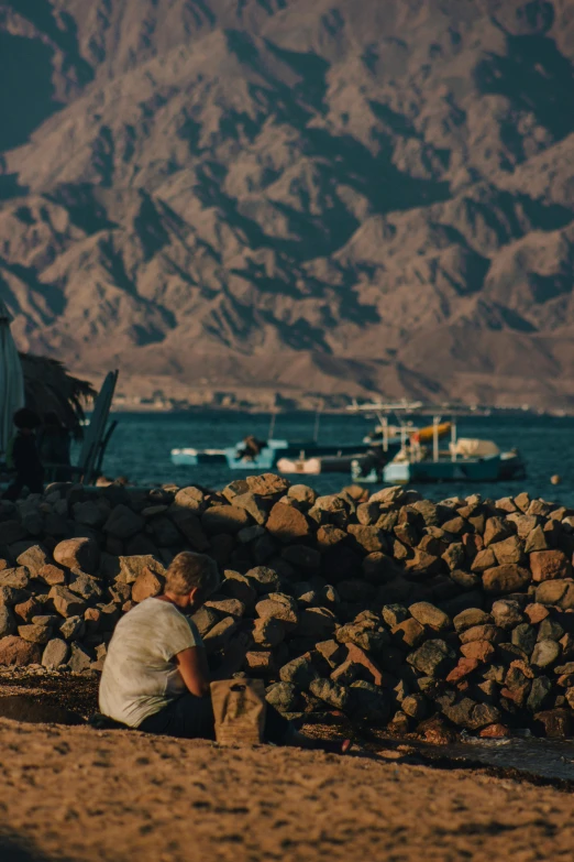 a person sitting on the ground by rocks near water