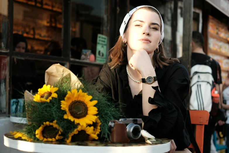 a young woman in headband sitting at a table with yellow sunflowers