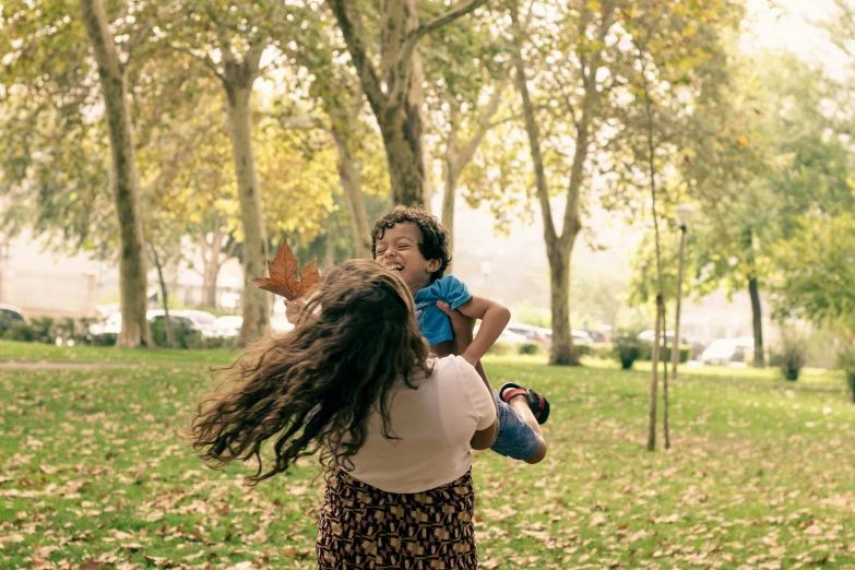 a woman holding a child with leaves flying by her