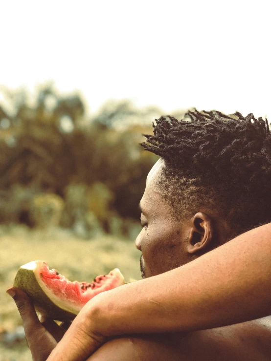 a man eating a piece of watermelon on a beach