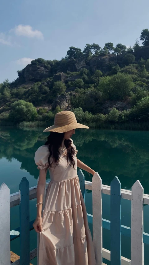 a woman in a dress standing on a bridge near water