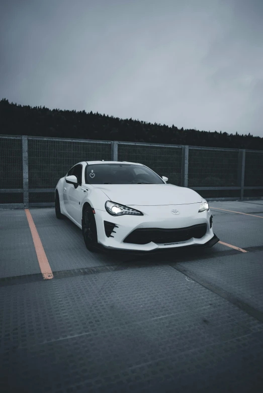 white sports car parked in a parking lot near a fence