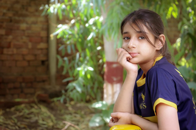 a girl in a blue and yellow soccer jersey sitting on a yellow stool