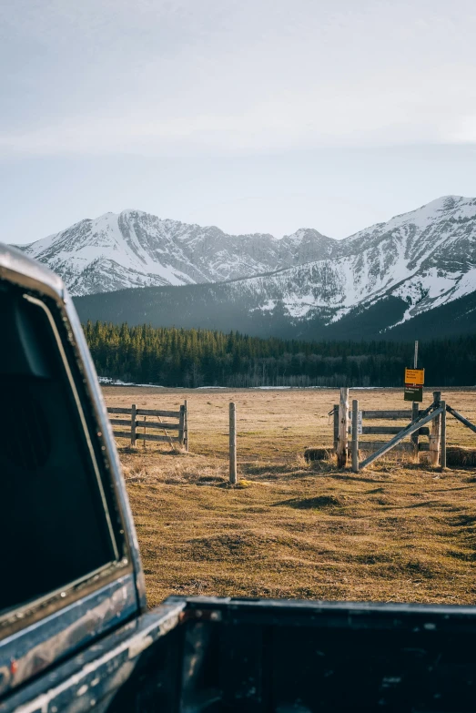 a truck sits in front of a wooden fence on a grassy field with mountains behind it