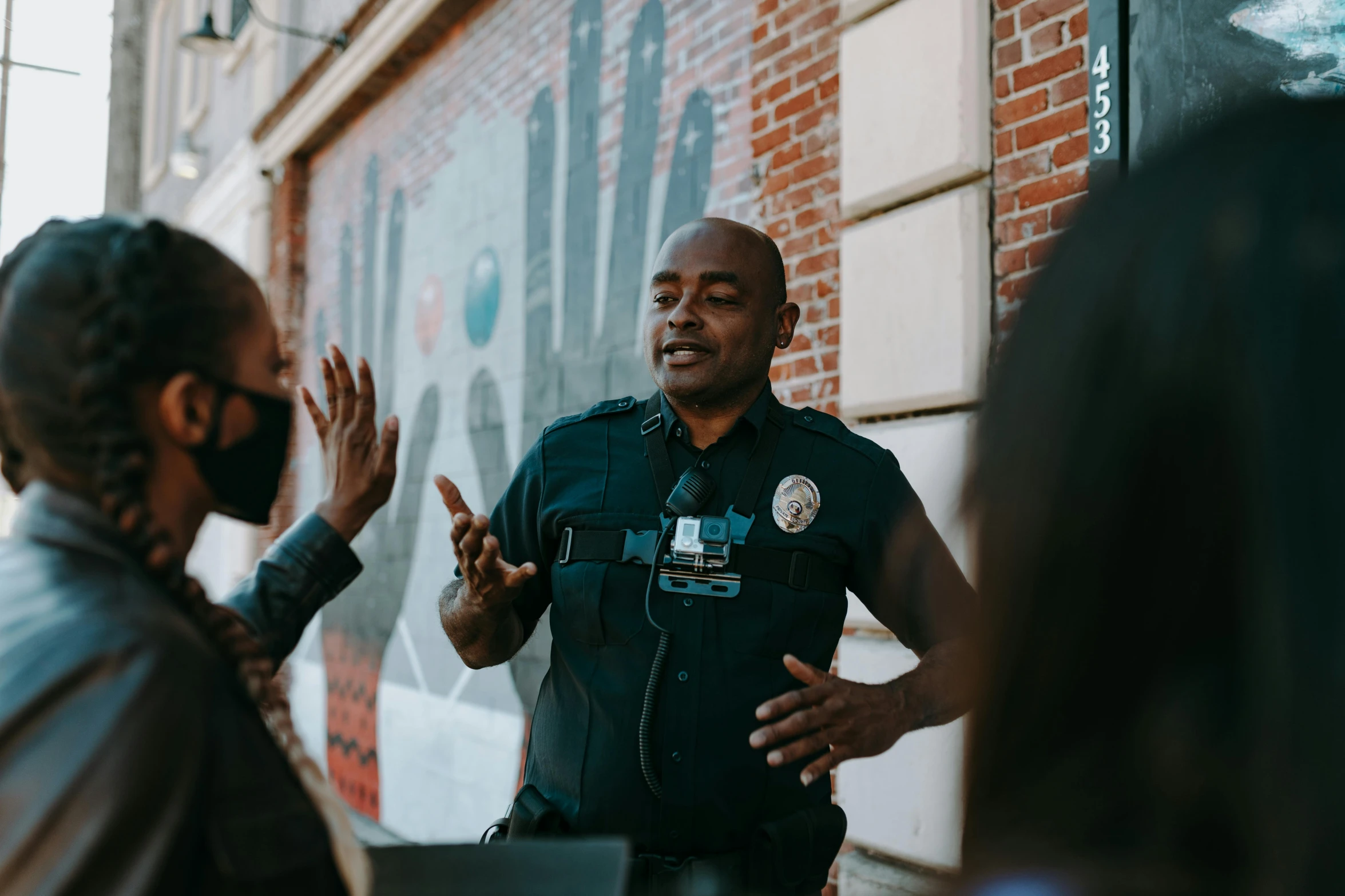 an officer speaking to a group of people standing in front of a brick wall