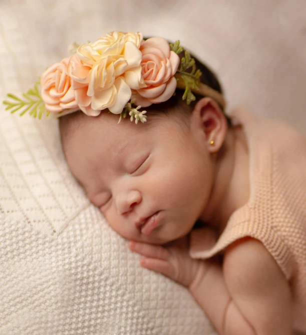 a baby wrapped in a wrap sleeps wearing a flower in it's head