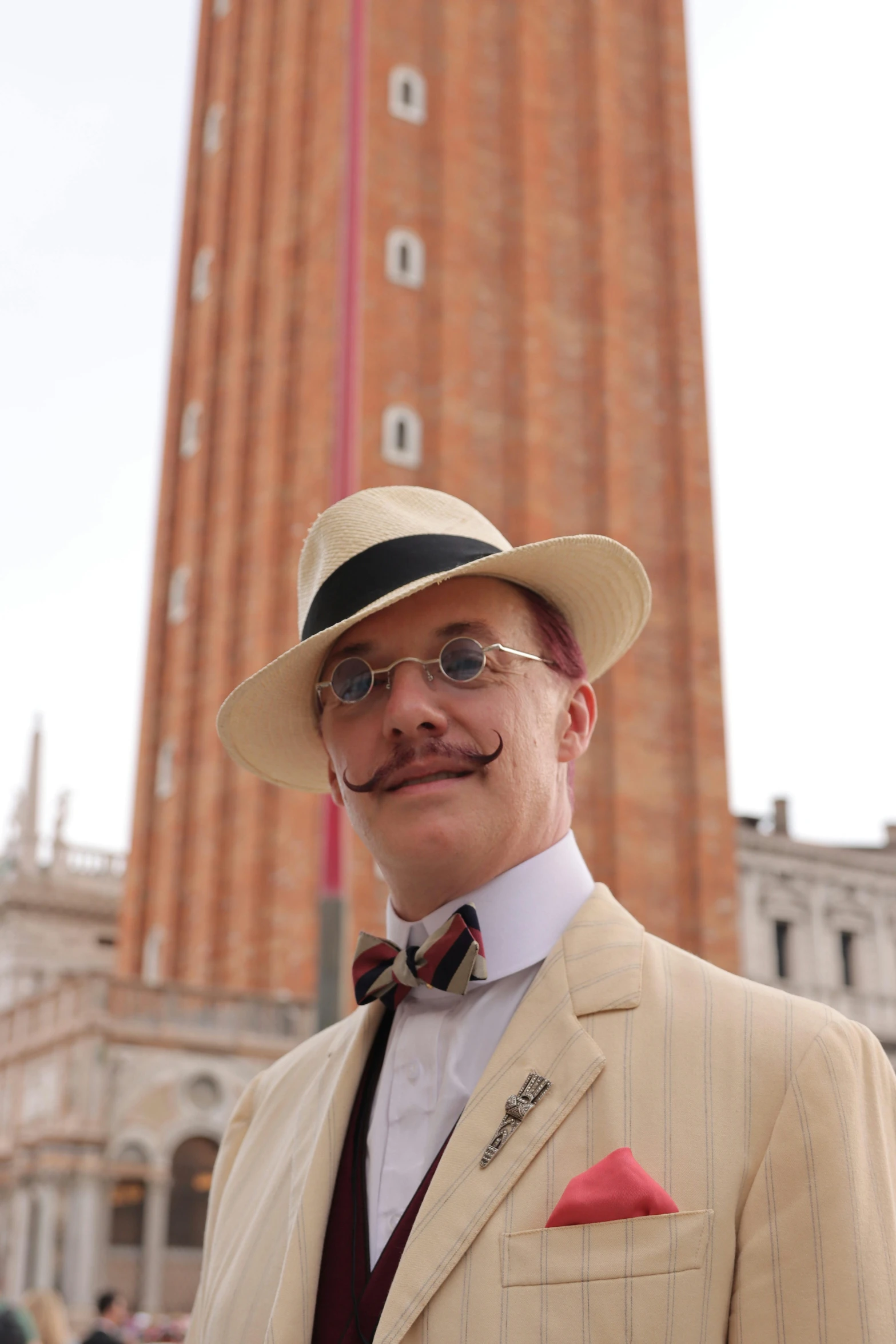 a man wearing a beige suit with a hat, striped tie and glasses