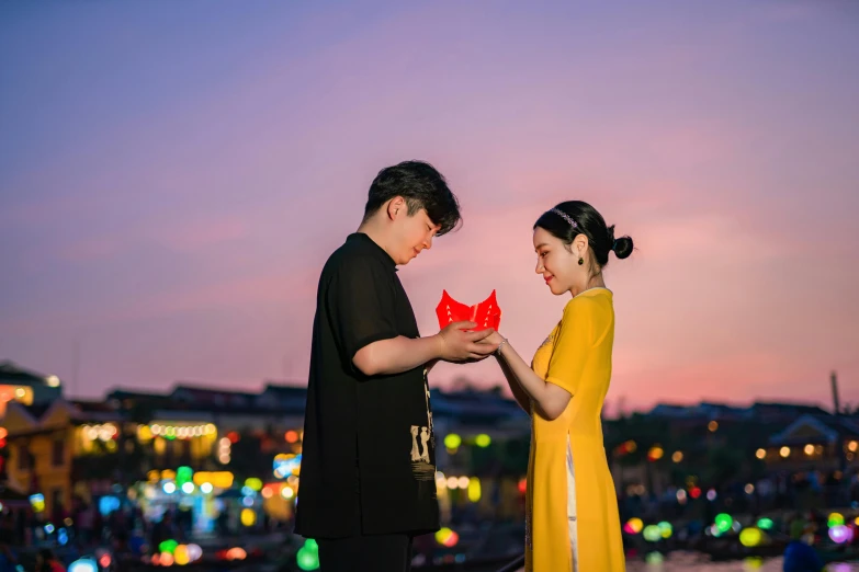 an engaged couple hold up red paper heart shapes