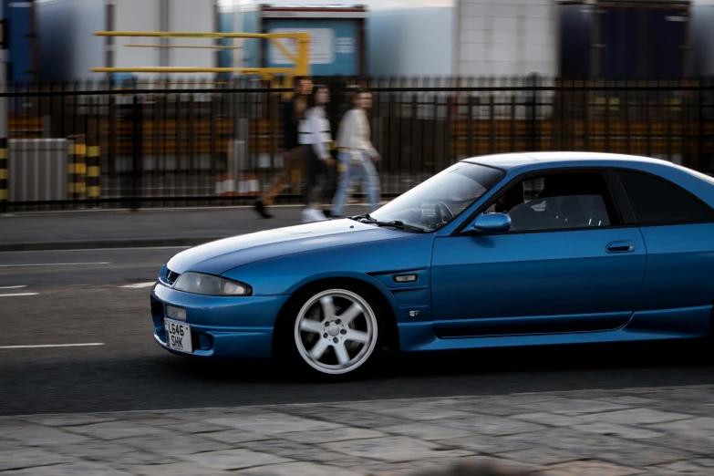 a blue car parked on the street in front of some pedestrians