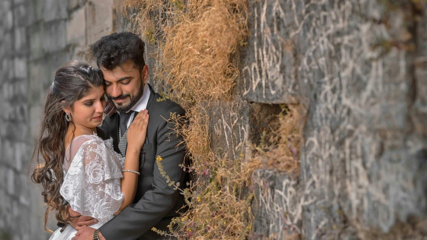 a beautiful young couple standing near the stone wall