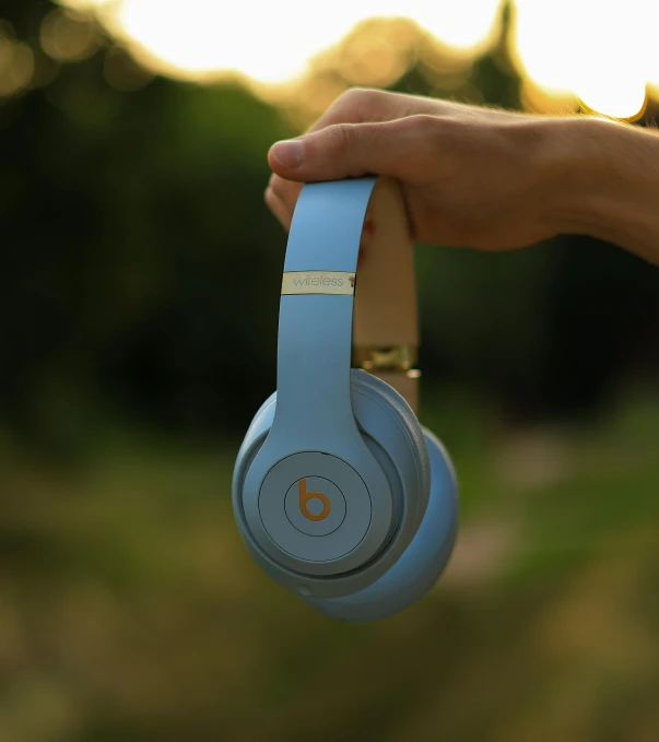 hand holding blue headphones near tree line in outdoors