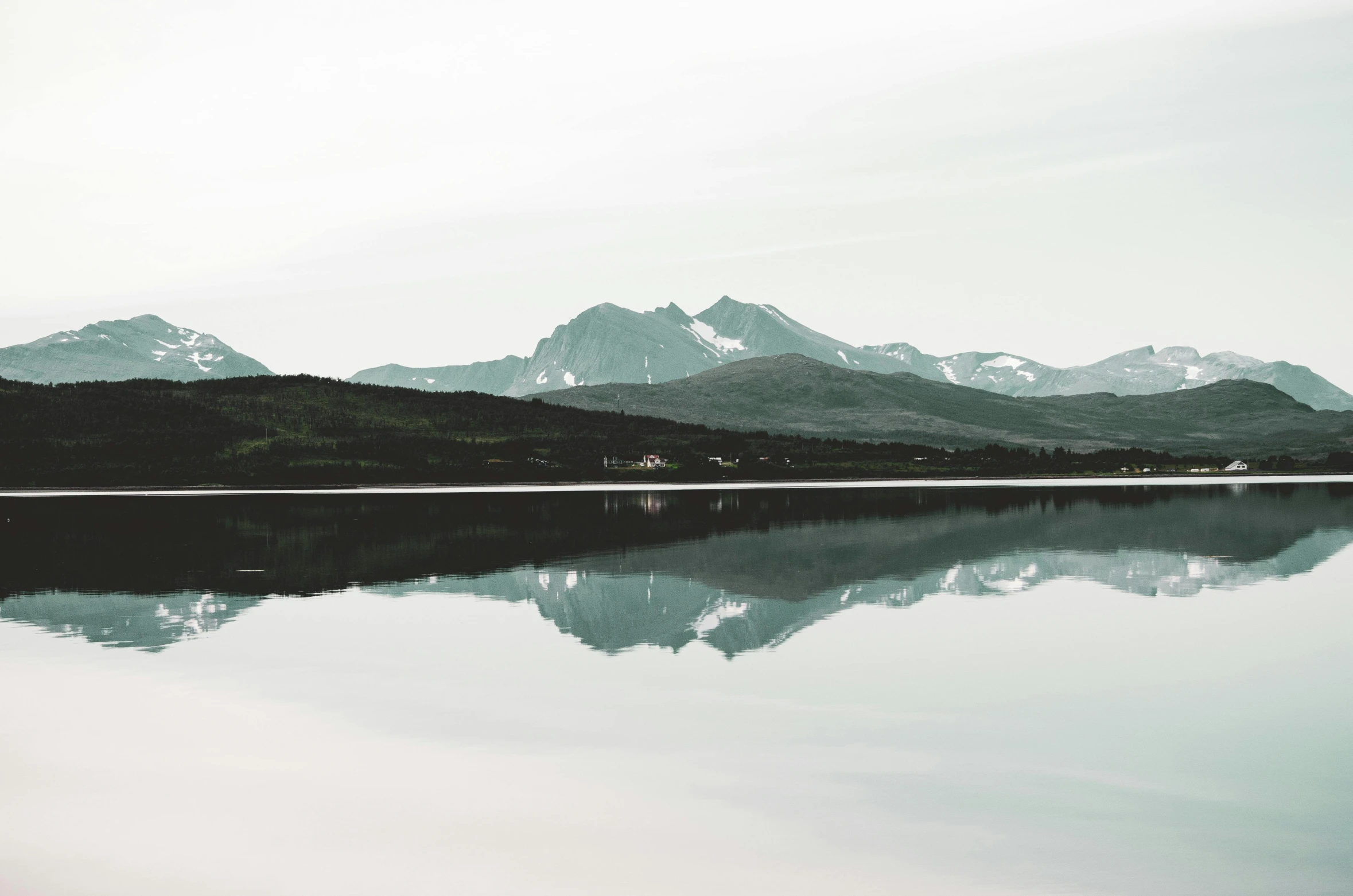 a mountain range sits above the water and reflects its surrounding mountains