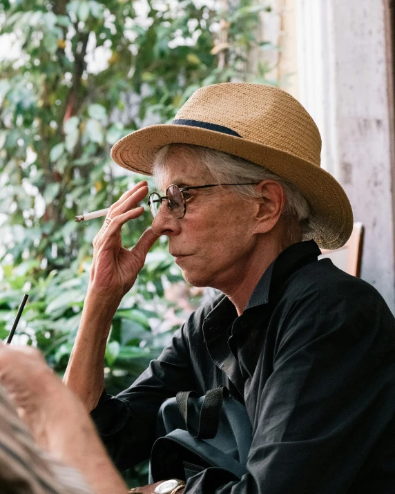 an older man smoking and sitting in front of some plants