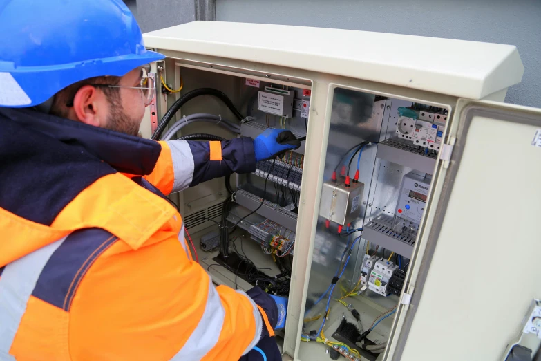 man fixing electrical wires inside of a white cabinet