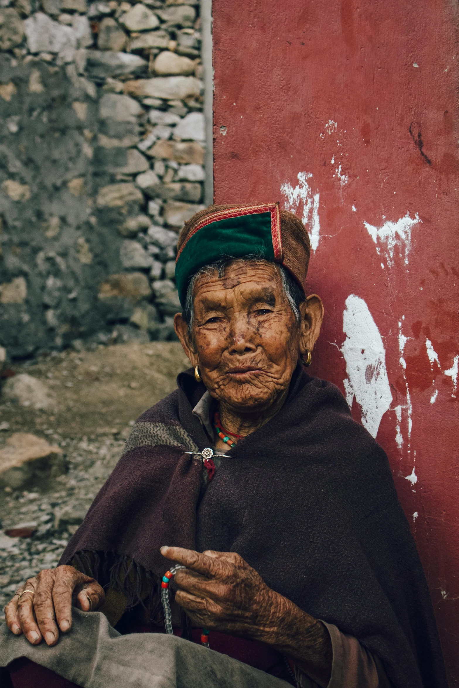 an older woman in head dress sits next to a wall