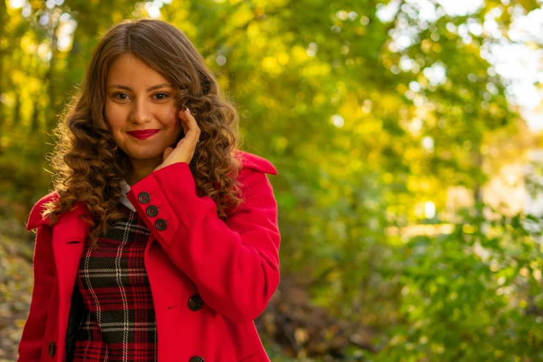 woman in red coat standing with cellphone near trees