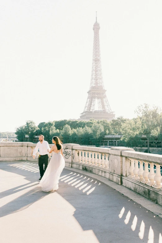 a man and woman are holding hands while walking near the eiffel tower