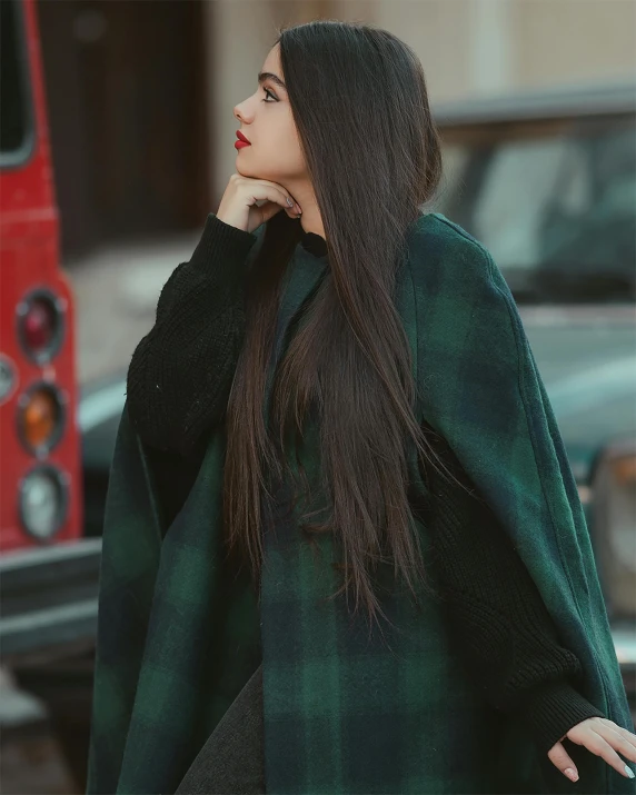 a woman wearing a green and black ponchle looking away from the camera