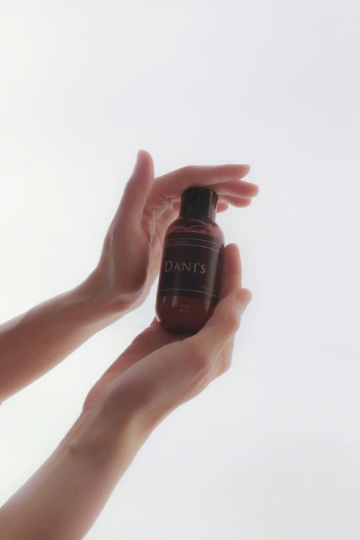 a hand holding a small bottle with brown liquid