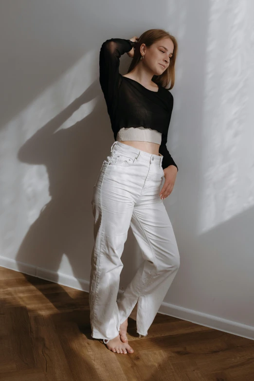 a woman leaning up against a wall in white pants