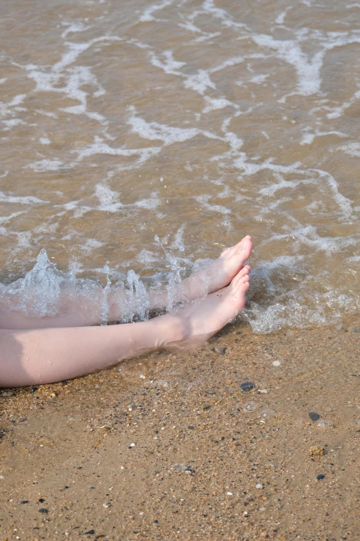 a person is lying on the beach with their feet in the water