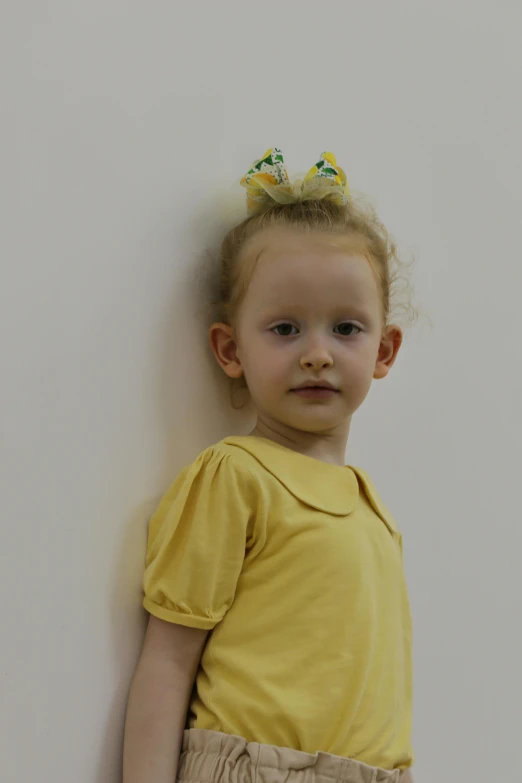  with large messy hair and a yellow top standing next to a wall
