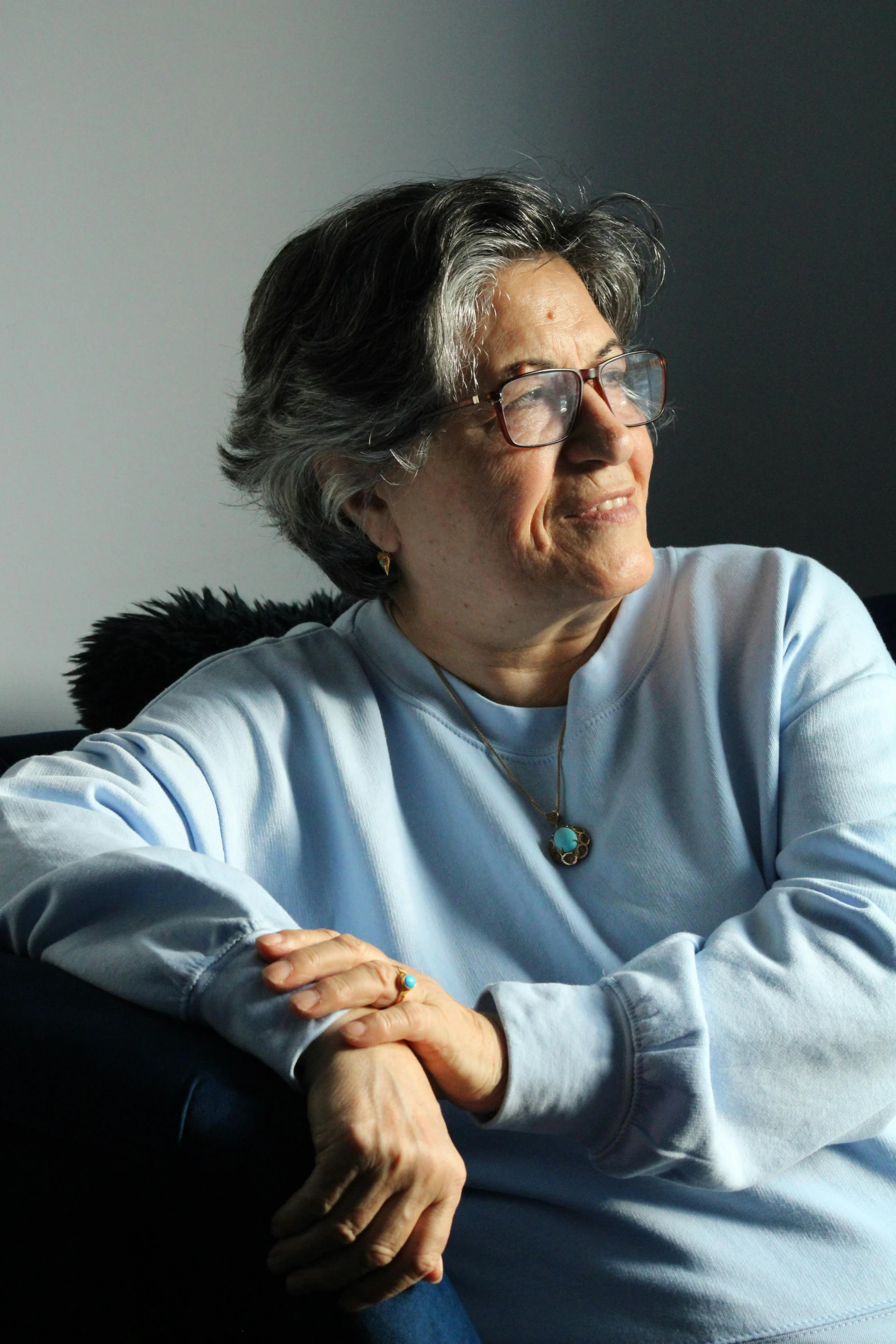 an older woman with glasses smiles as she sits on the couch