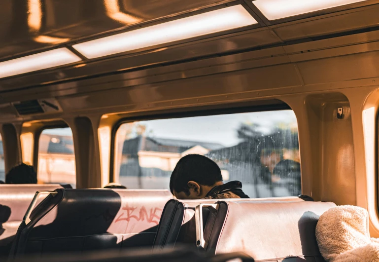 a person sits with their back turned to the side of the train, looking out the window