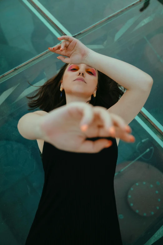 a young woman in a black dress is looking up with her hand to the side