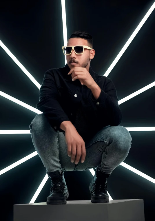 a man posing for a portrait wearing sunglasses and standing in front of a black backdrop