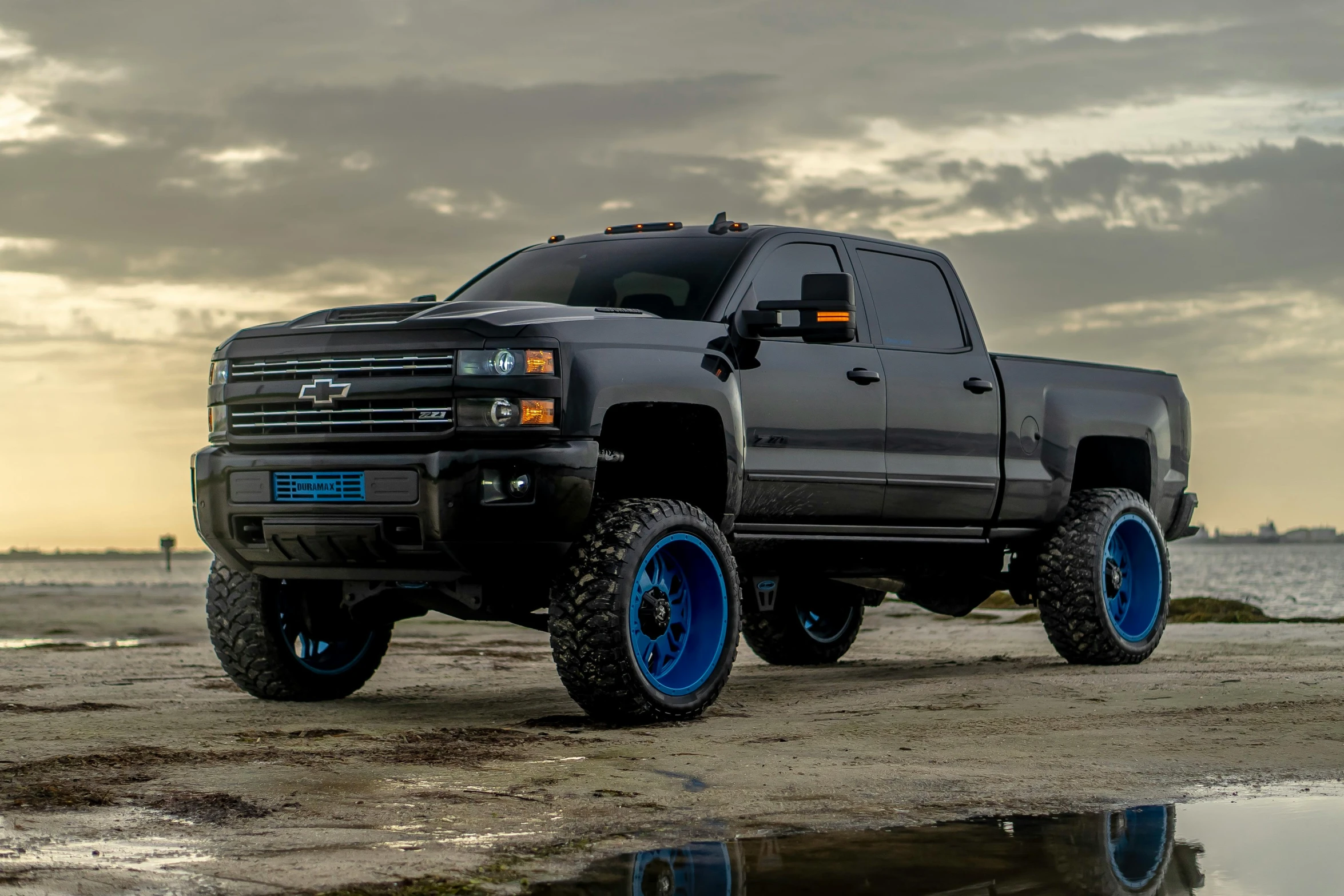 a truck parked next to water on a rocky beach