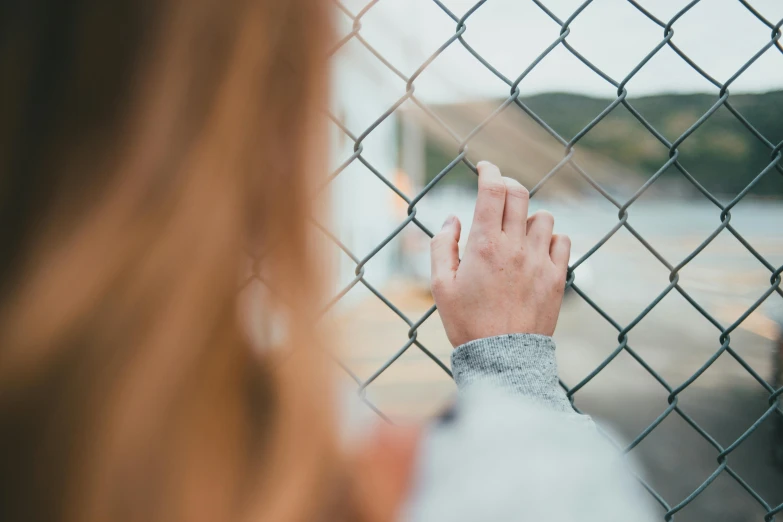 a person behind a fence with their hand on a fence