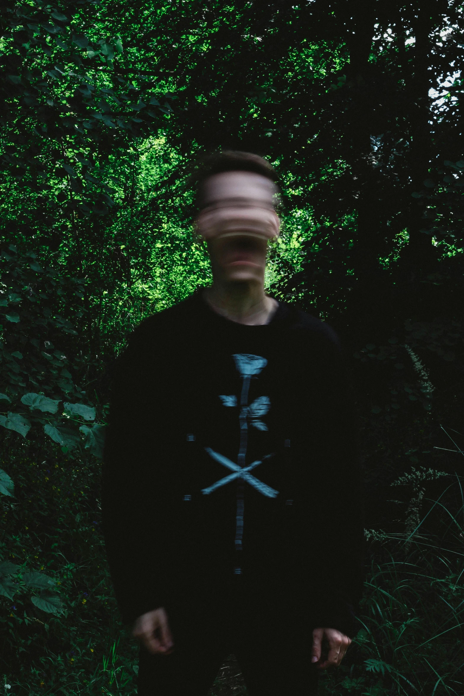 man standing in front of trees and bush wearing a hooded sweatshirt