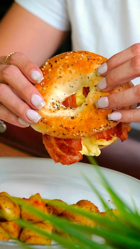 a woman holding half of a bacon and cheese bagel