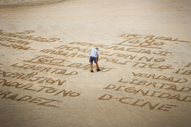 an individual in the distance standing next to writing on a sand covered beach