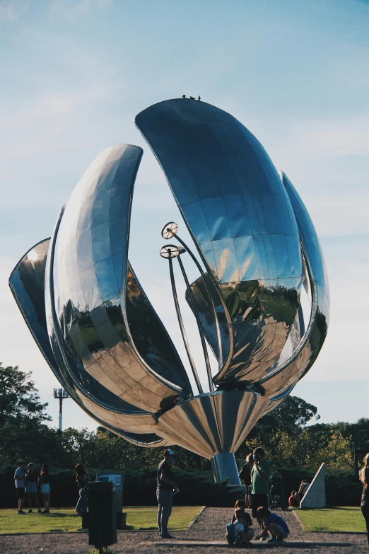 two people are sitting on the ground under a giant metal sculpture