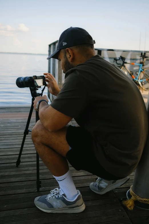 a man squatting down to take a picture of his tripod on the dock