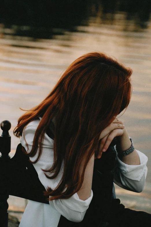 a red headed woman sitting next to the water